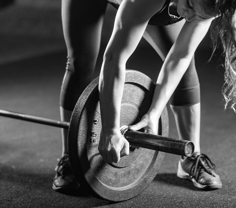 Black and white image of a women loading a weighted plate to a bar