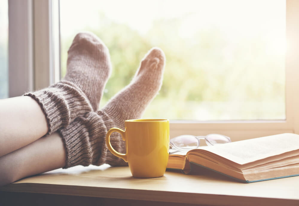 legs and feet resting on a table with a cup of tea and book